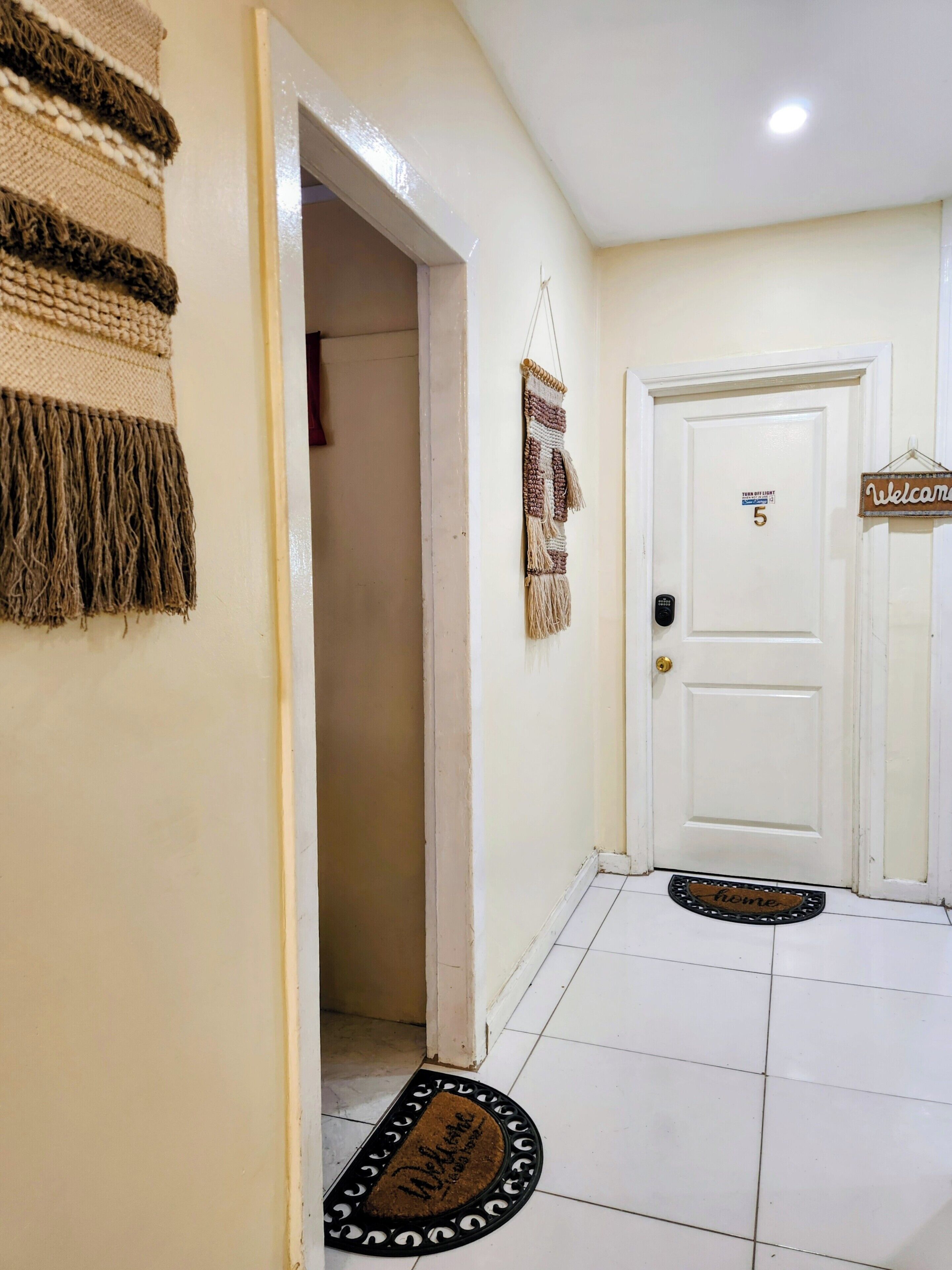 A hallway with a white door marked '5', a welcome sign, and a doormat with 'home' written on it.