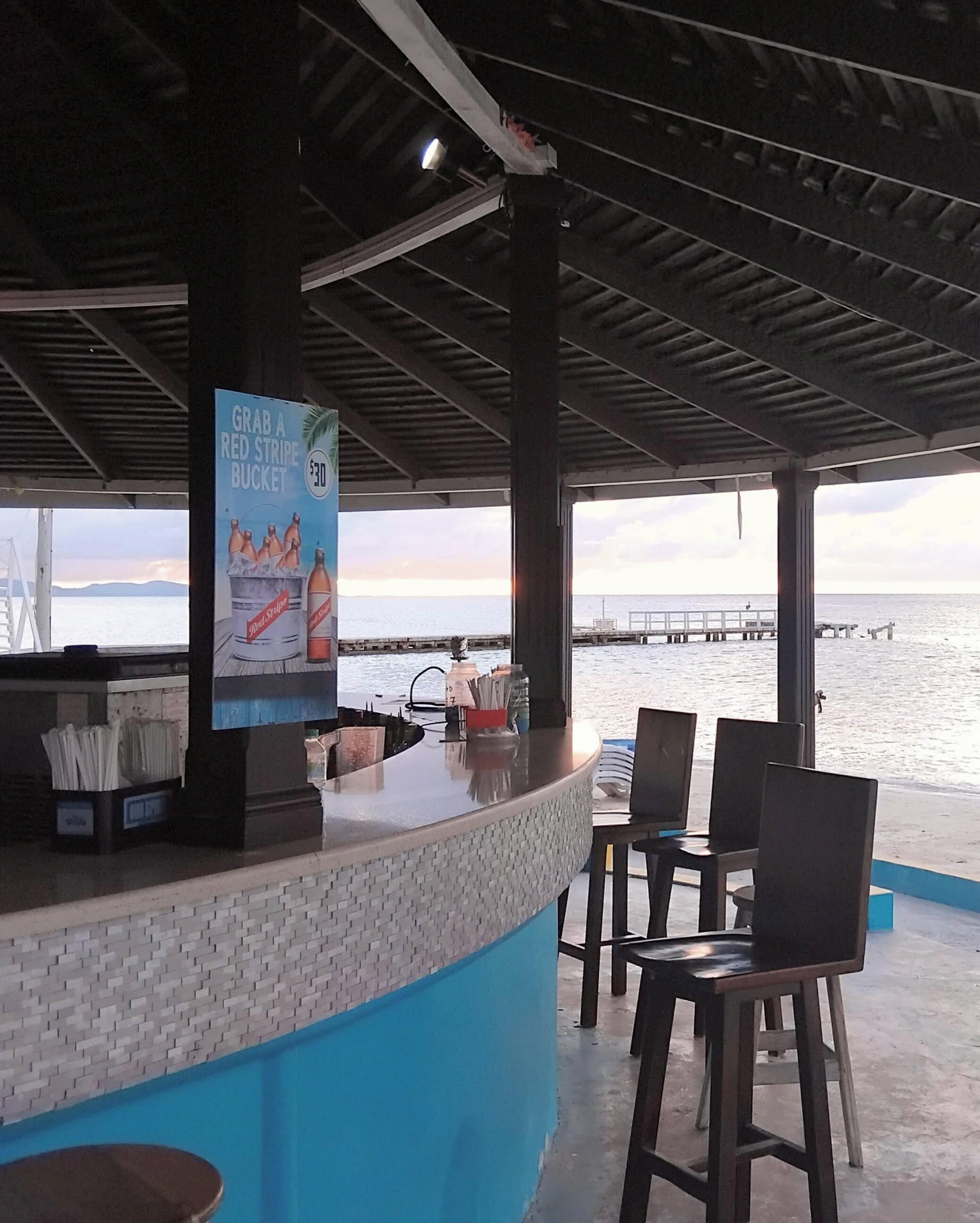 Eine Außenbar mit Blick auf das Meer und eine Mole im Hintergrund.