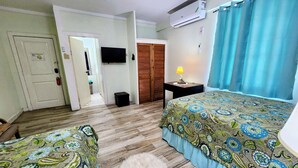 A bedroom with two beds, a TV, an air conditioner, a lamp, and a door leading to a hallway. - Hip Strip Vibe (Montego Bay)