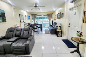 A living room with a sofa, a dining area with chairs, a ceiling fan, and a door with a number.