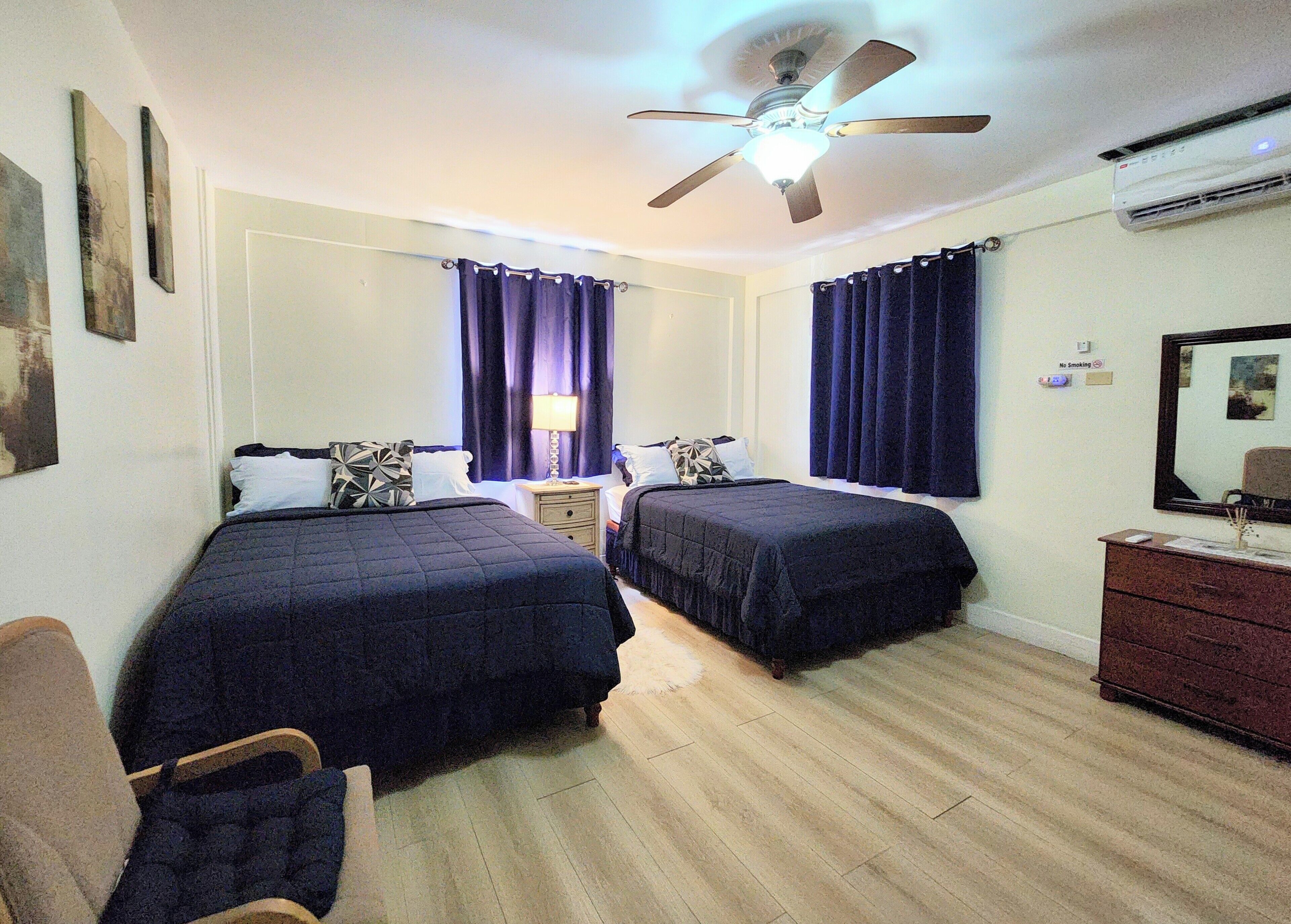 A hotel room with two beds, a ceiling fan, a nightstand, a dresser, and a mirror.