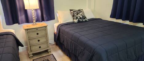 Un dormitorio con cama, mesitas de noche, lámpara, alfombra y cortinas.