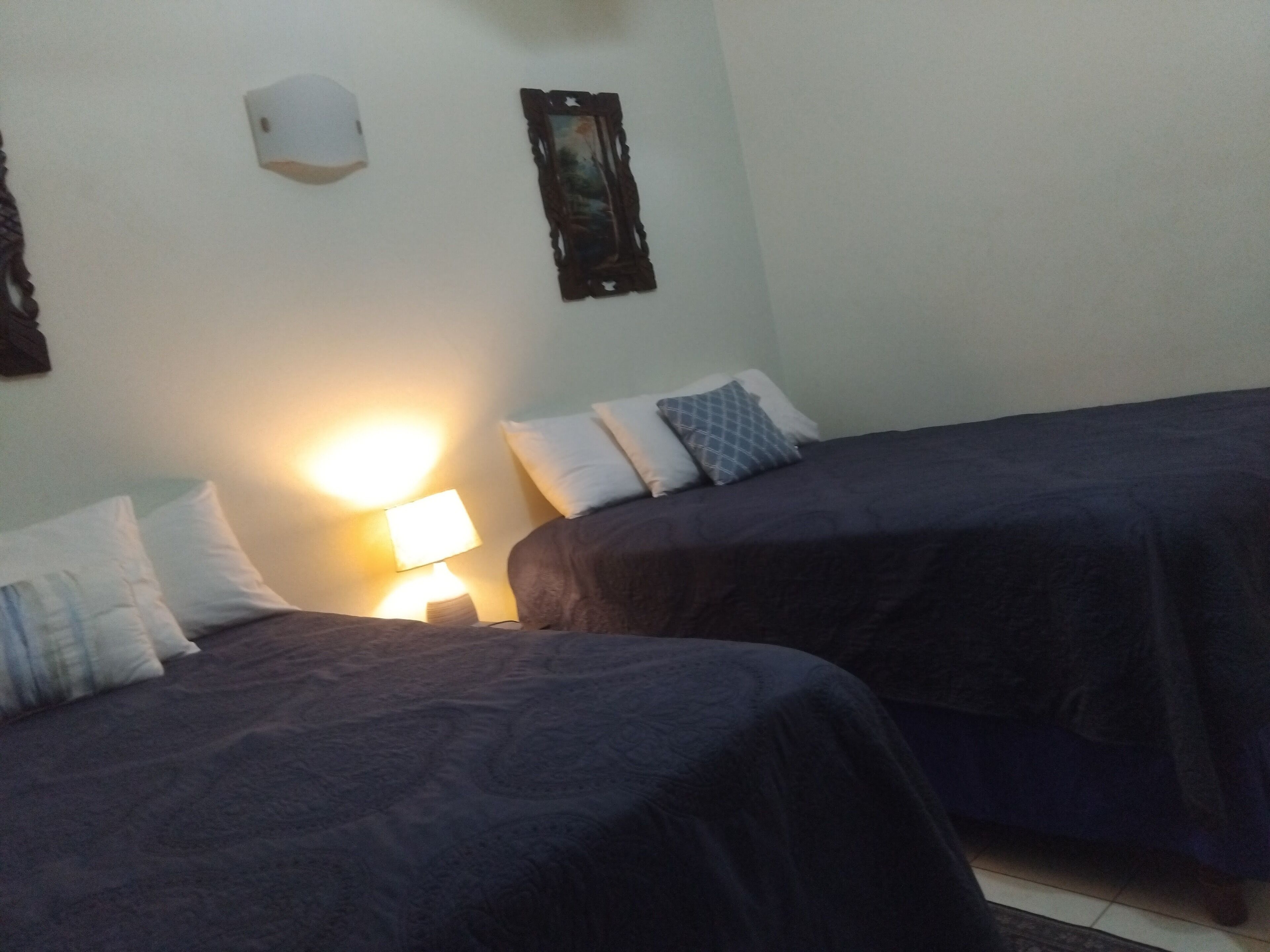 A hotel room with two beds, a nightstand with a lamp, and a wall-mounted air conditioner.