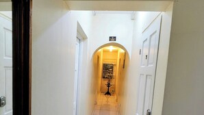 A hallway with white tiled floors, white walls, and a door at the end. - Hip Strip Vibe (Montego Bay)
