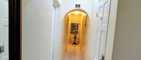 A hallway with white tiled floors, white walls, and a door at the end.