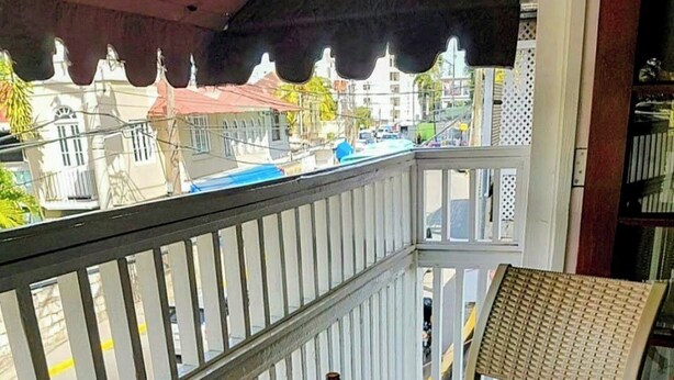 A balcony with a round table and a chair, a bottle on the table, and a view of buildings in the background. - Hip Strip Vibe (Montego Bay)