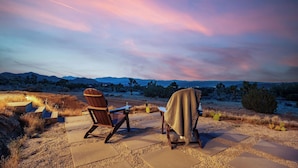 Eine Terrasse mit zwei Adirondack-Stühlen, einem Tisch und einer Decke.