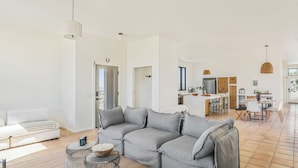 Ein geräumiger Wohnbereich mit grauem Sofa, einem Esstisch und einer Küche im Hintergrund.