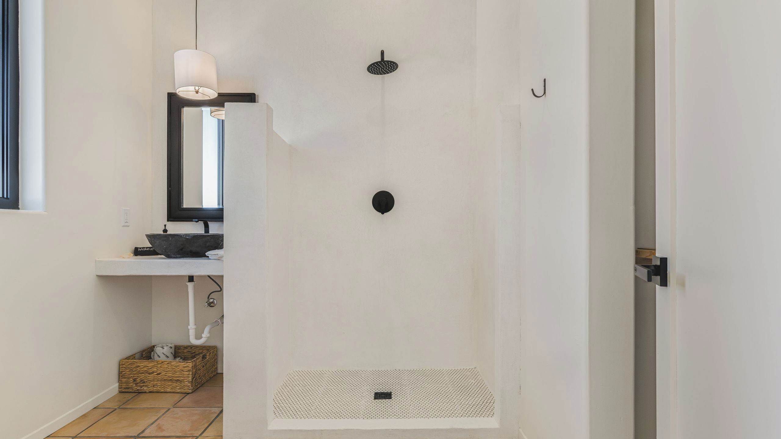 Une salle de bain avec un lavabo blanc, un miroir, une serviette, une pomme de douche et un porte-serviettes.