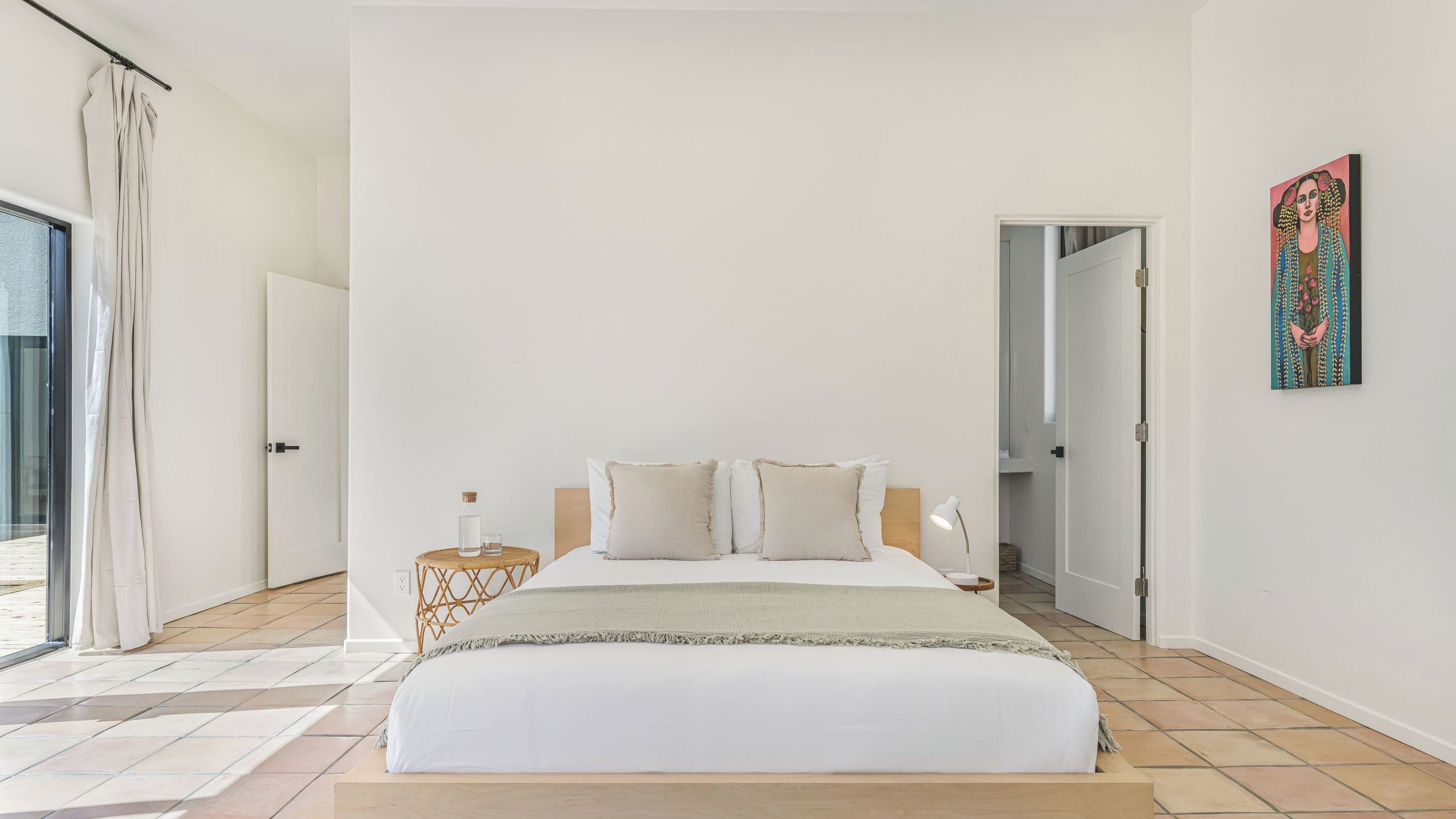 A bedroom with a bed, bedside table, lamp, and a painting on the wall.