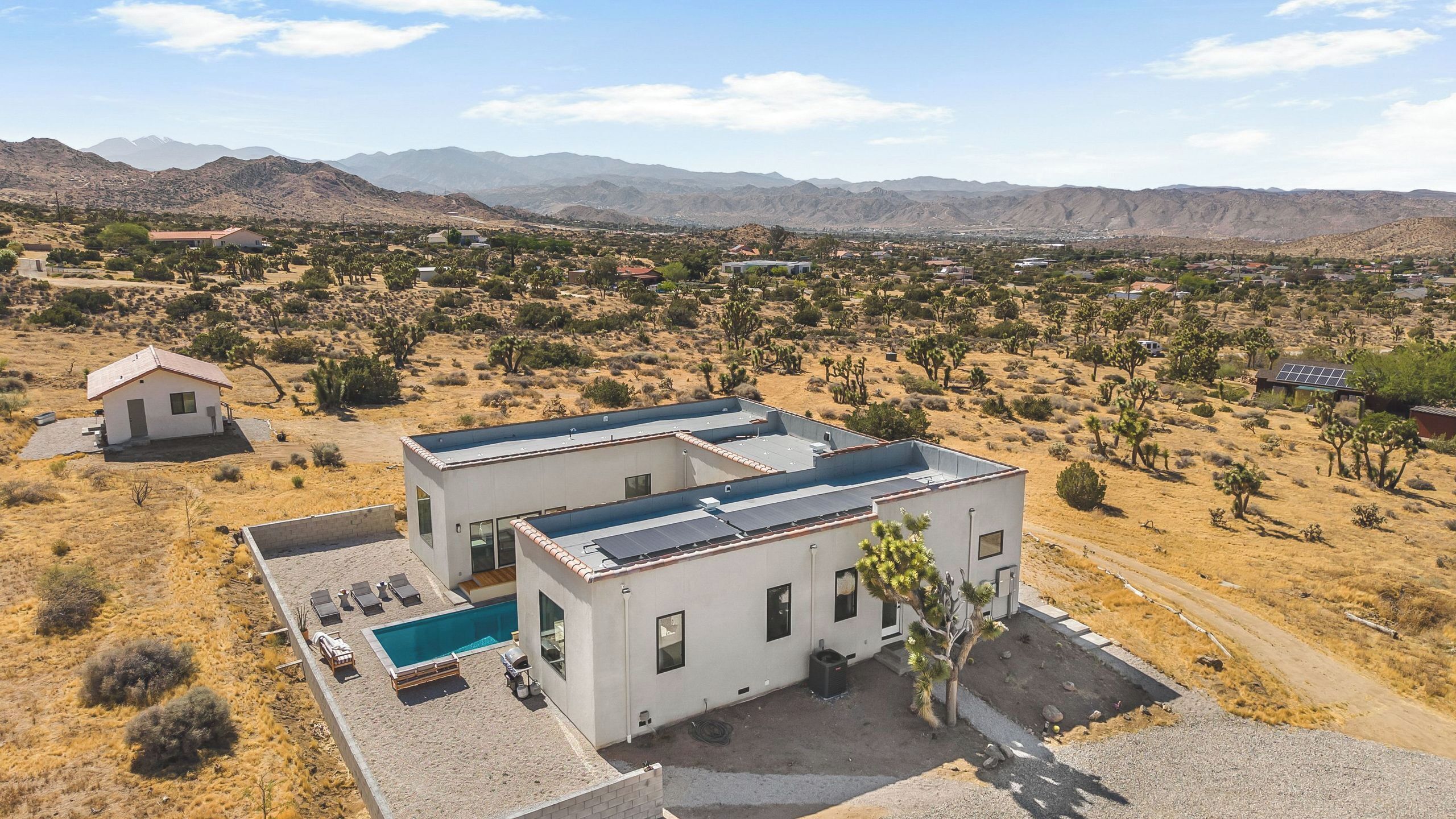 A modern two-story house with a swimming pool, surrounded by desert landscape and mountains.