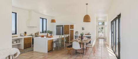 A modern kitchen with a central island, a dining area with chairs, and a view through a glass door.
