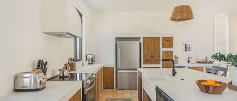 A modern kitchen with a stainless steel refrigerator, a toaster, and a dishwasher. There is a wooden cabinet and a window above the sink.