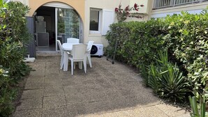 Un patio con una mesa y sillas, un pequeño jardín y la entrada de un edificio.
