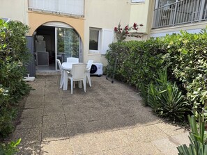 Eine Terrasse mit Tisch und Stühlen, ein kleiner Garten und ein Gebäudeeingang.