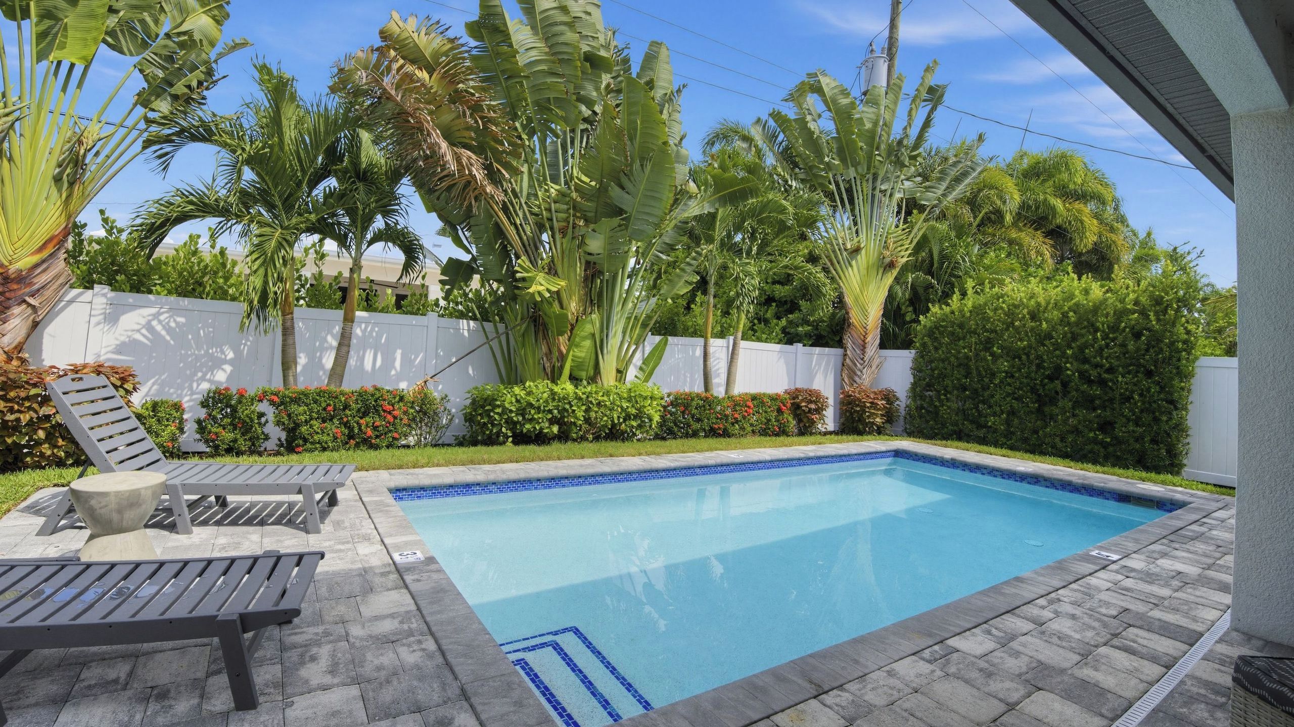 A swimming pool with lounge chairs and a white fence in the background.