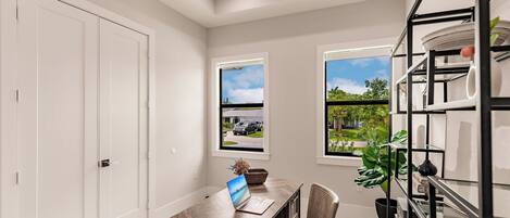 A room with a desk, chair, laptop, two windows with views, and a shelving unit.