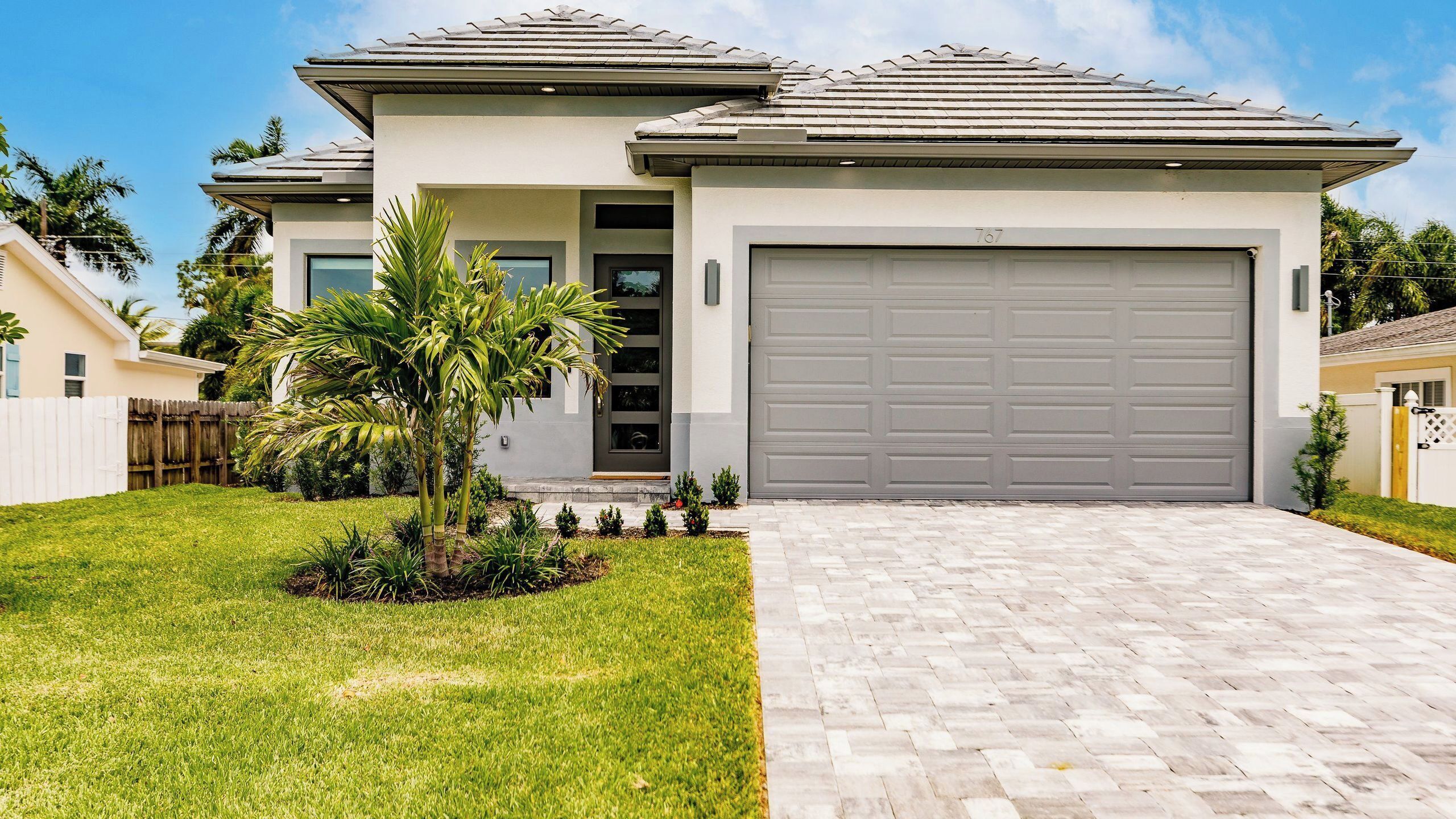 A modern two-story house with a garage, a well-maintained lawn, and a palm tree.