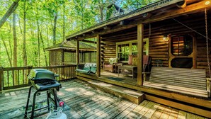 Une cabane en bois avec une véranda, un barbecue et un banc.