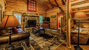 L’intérieur d’une cabane en rondins, avec une cheminée, des meubles en cuir, un plafond en bois et un téléviseur fixé au mur.