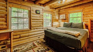 Une chambre à coucher située dans une cabane en rondins, avec un lit, deux fenêtres, une lampe et un tapis.