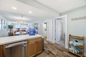A spacious kitchen with a central island, wooden cabinets, and a stainless steel dishwasher. - Above the Tide | Oceanfront | Community Pool (Nags Head)