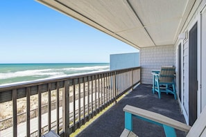 A balcony with a view of the ocean, a wooden deck, and a small seating area with chairs. - Above the Tide | Oceanfront | Community Pool (Nags Head)