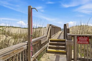 A wooden boardwalk leading to a beach with a warning sign about no walking or climbing on the dunes. - Above the Tide | Oceanfront | Community Pool (Nags Head)