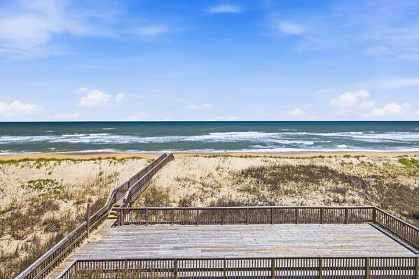A beach view with a wooden boardwalk leading to the ocean. - Above the Tide | Oceanfront | Community Pool (Nags Head)