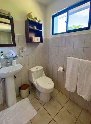 A bathroom with a toilet, sink, and shelves above the toilet. - Welcome to CnH Costa Verde: Charming 1-bedroom condo with AC in sunny Coco (Coco)