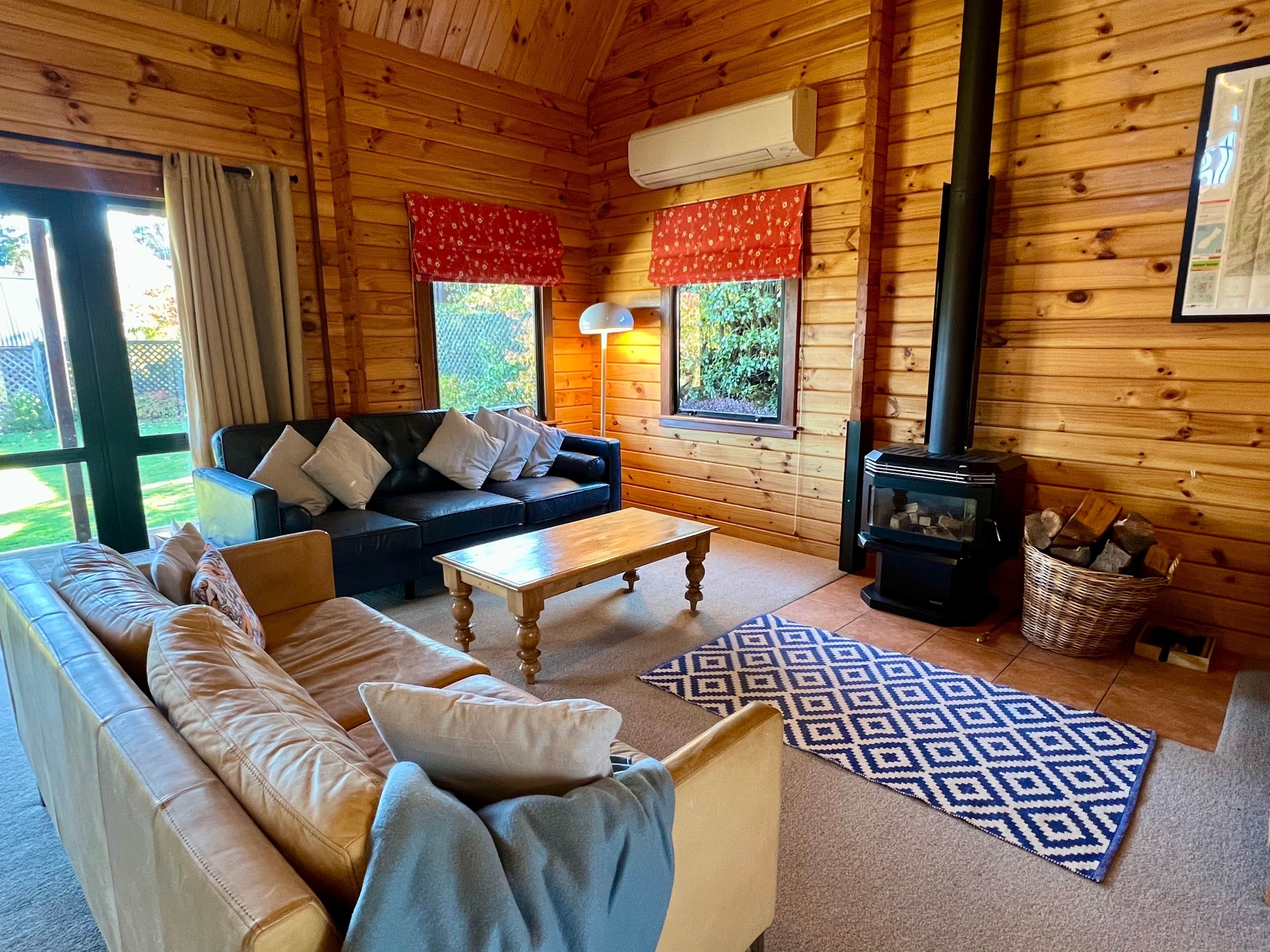 L’intérieur d’un chalet accueillant, avec un canapé, une table basse, une cheminée et une fenêtre avec des rideaux.