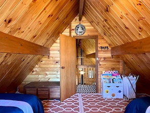 Une chambre mansardée avec des murs en bois, un lit, une petite table et une boîte à jouets pour enfants.