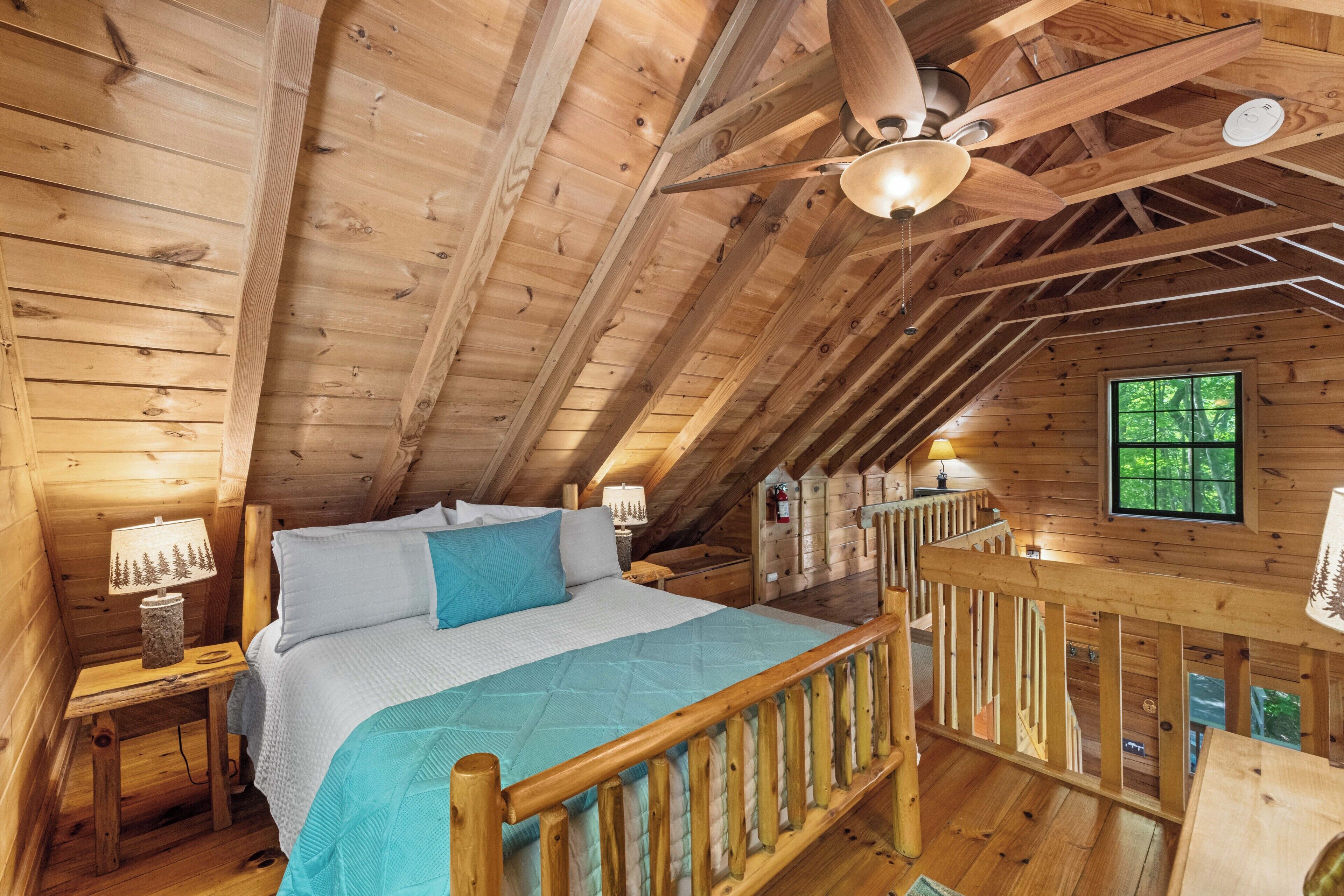 A wooden cabin bedroom with a bed, nightstands, a ceiling fan, and a window.