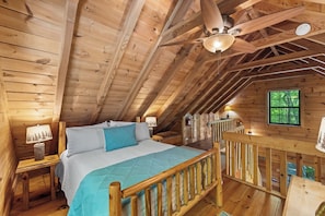 A wooden cabin bedroom with a bed, nightstands, a ceiling fan, and a window. - A Bird's Eye View - Pet-Friendly Cabin in Cherry Log (Cherry Log)