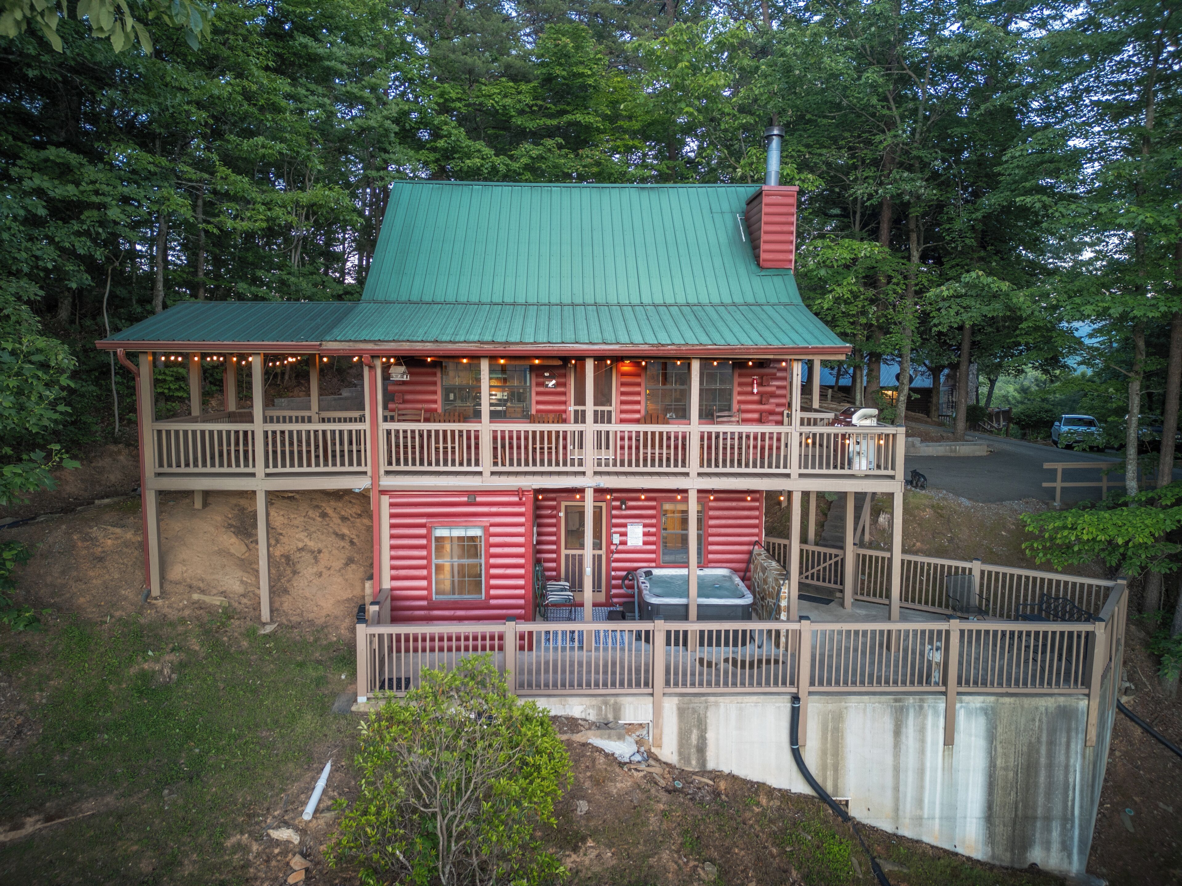 A two-story log cabin with a green roof, a balcony on the upper floor, and a fenced front yard.