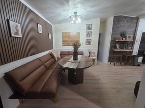 A modern living room with a brown leather sofa, a wooden dining table, and a ceiling light fixture.
