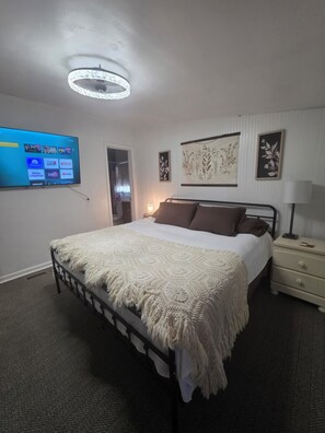 A neatly arranged bedroom with a bed, bedside tables, a wall-mounted TV, and decorative wall art.