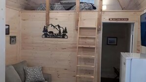 A cozy cabin interior with a bunk bed, a sofa, a coffee table, and a refrigerator. - The Denali Cabin w/ Queen Bed (Seward)