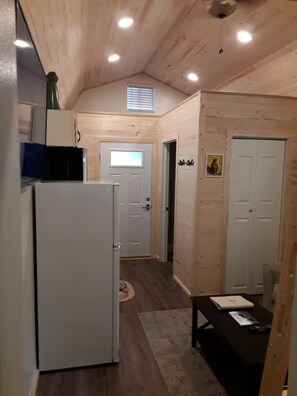 A compact kitchen with a refrigerator, a window, and a door leading to another room.