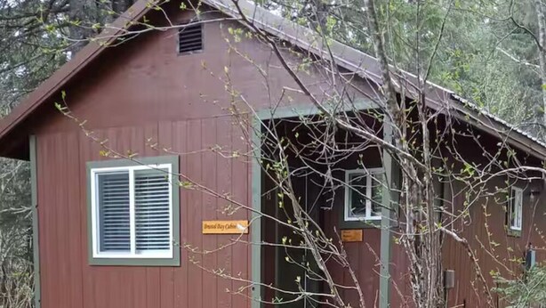 Eine kleine, eingeschossige Holzhütte mit einer Haustür und einer kleinen Veranda mit Stufen.