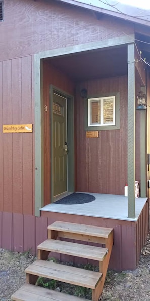 Une cabane en bois avec une porte verte, un petit porche et une enseigne indiquant « Bristol Bay Cabin ».