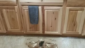 A kitchen with wooden cabinets, a stainless steel sink, and a coffee-themed placemat. - The Sitka Cabin w/ King Bed (Seward)