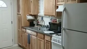 A kitchen with wooden cabinets, a stainless steel sink, a microwave, and a white refrigerator. - The Sitka Cabin w/ King Bed (Seward)
