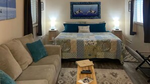 A cozy bedroom with a bed, a sofa, a ceiling fan, and a nightstand with a lamp. - The Sitka Cabin w/ King Bed (Seward)