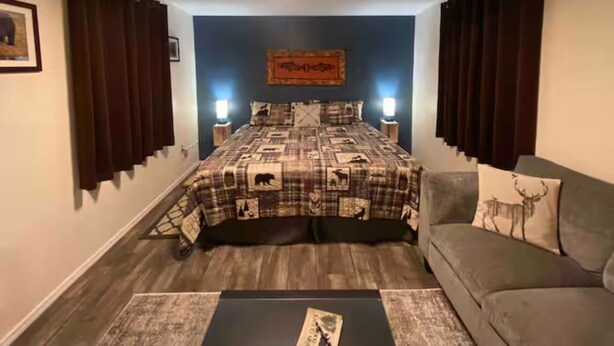 A bedroom with a bed, a sofa, a rug, and a wall with a framed picture. - The Kodiak Cabin w/ King Bed (Seward)