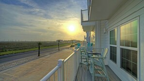 A balcony with chairs, a railing, and a view of a road and distant buildings. - Vacation Heaven by Avantstay North Padre Stay Gulf Views + Pool Access Near Whitecap Beach (Corpus Christi)