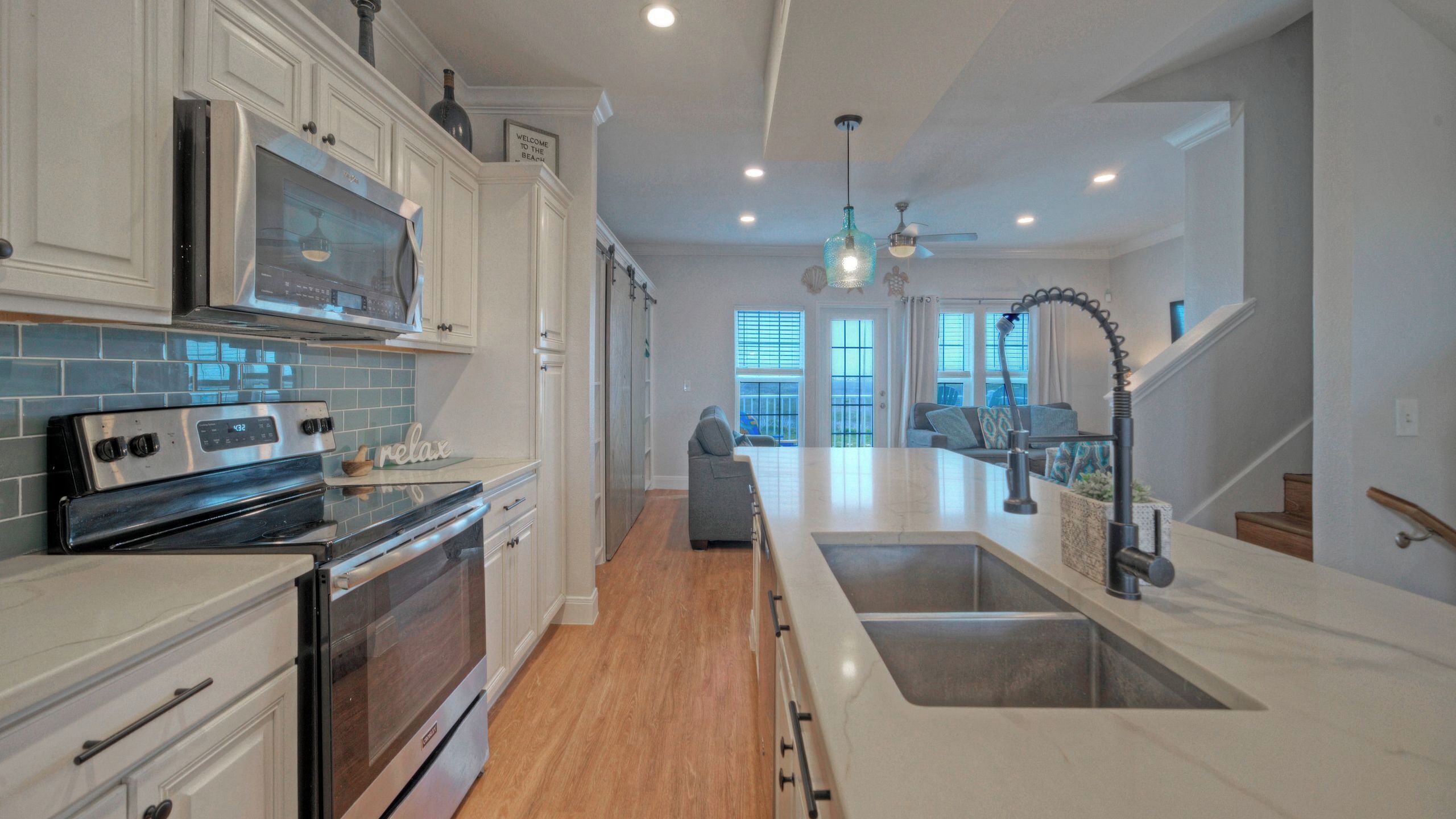 A modern kitchen with stainless steel appliances, a large island with a sink, and a view to the living area.
