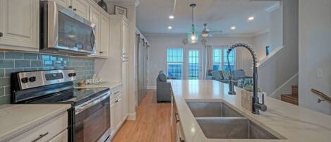 A modern kitchen with stainless steel appliances, a large island with a sink, and a view to the living area.