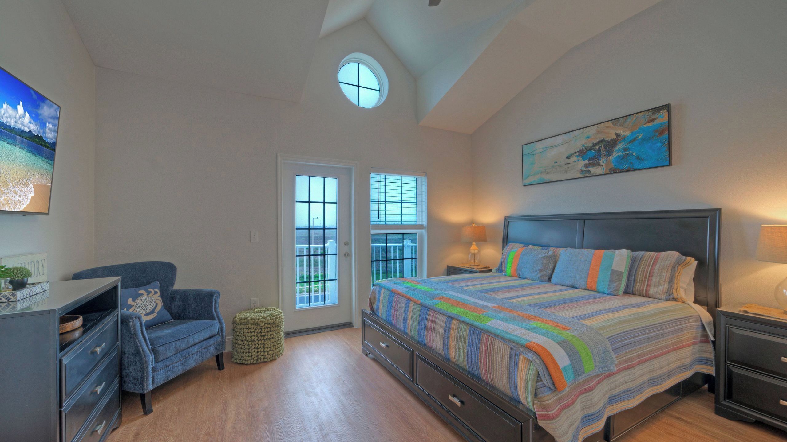 A bedroom with a bed, a desk, a chair, a window, and a painting on the wall.