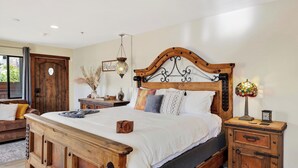 A bedroom with a wooden headboard, a bed with white linens, a nightstand with a lamp, and a wooden dresser. - Red Rock Duo by Avantstay - Sleeps 8, 2 Sedona Retreats With Mountain Views, Heart of West Sedona (Sedona)